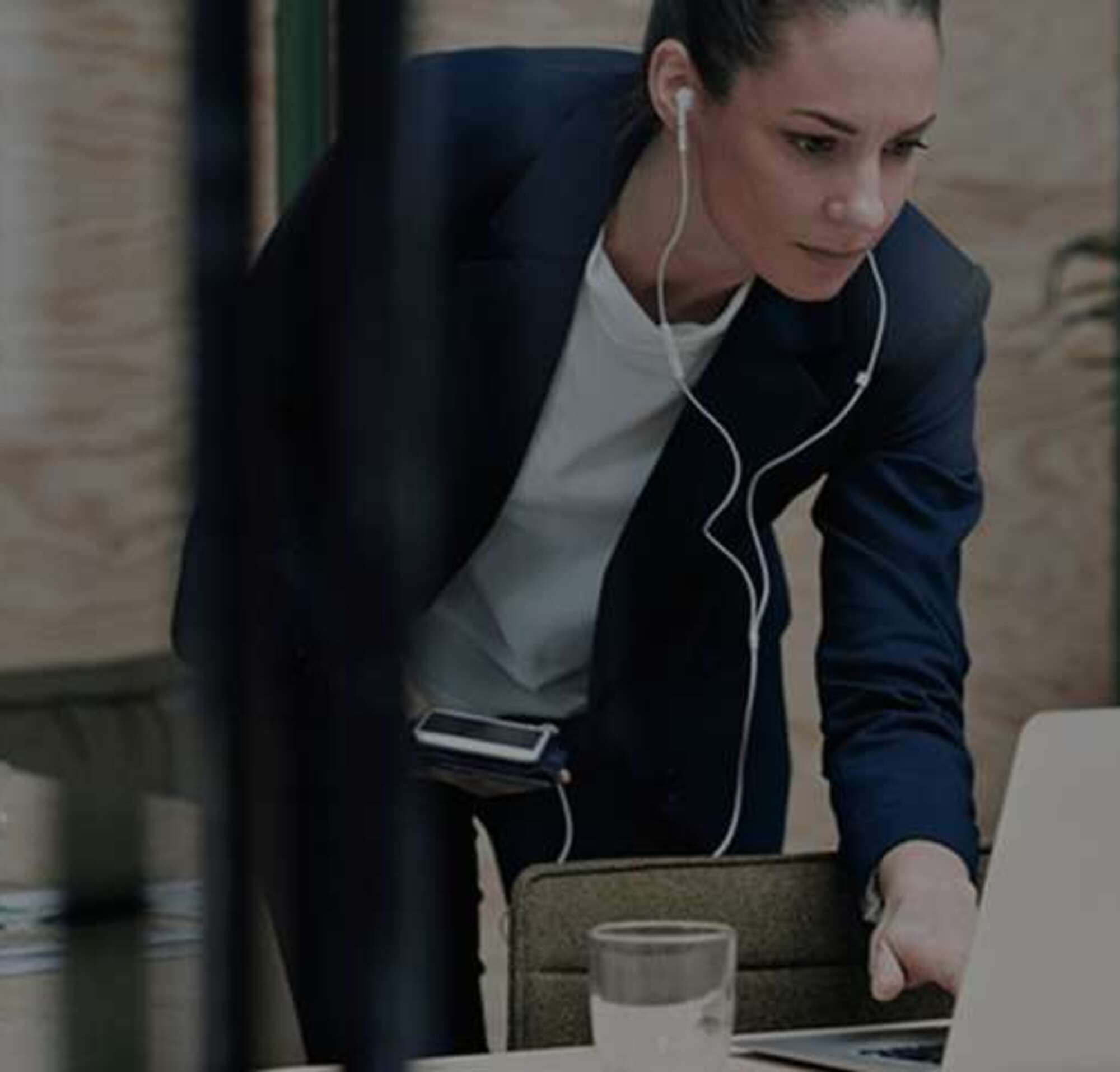Mujer con auriculares trabajando en una laptop y con su teléfono en las manos.